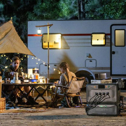 Two people camping outdoors with an RV, lights, and a BLUETTI power station.